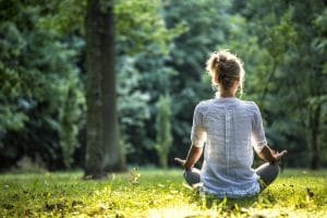 Une femme assise en méditation dehors fait son yoga thérapeutique | thérapie et yoga thérapie - Sutton, Québec, Canada, France, Belgique, Suisse, Maroc | Liance